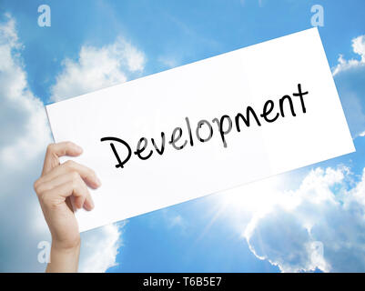 Development Sign on white paper. Man Hand Holding Paper with text. Isolated on sky background Stock Photo