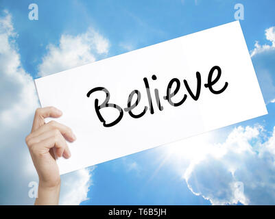 Believe Sign on white paper. Man Hand Holding Paper with text. Isolated on sky background Stock Photo