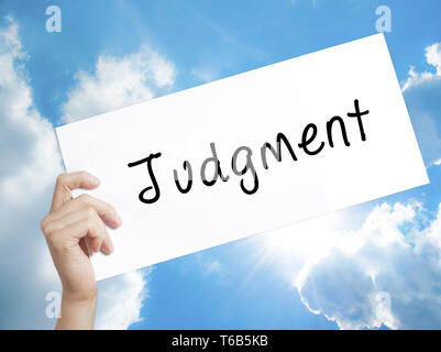 Judgment Sign on white paper. Man Hand Holding Paper with text. Isolated on sky background Stock Photo