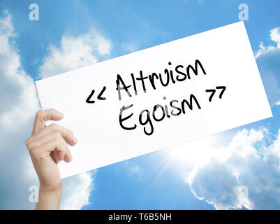 Altruism - Egoism Sign on white paper. Man Hand Holding Paper with text. Isolated on sky background. Stock Photo