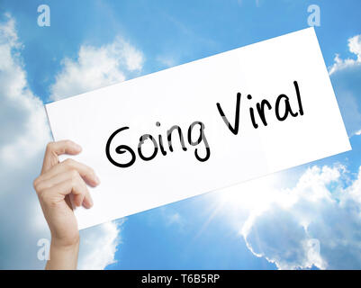 Going Viral Sign on white paper. Man Hand Holding Paper with text. Isolated on sky background Stock Photo