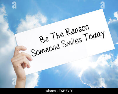 Be The Reason Someone Smiles Today  Sign on white paper. Man Hand Holding Paper with text. Isolated on sky background Stock Photo