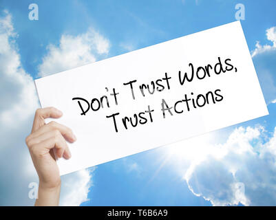 Don't Trust Words, Trust Actions Sign on white paper. Man Hand Holding Paper with text. Isolated on sky background Stock Photo