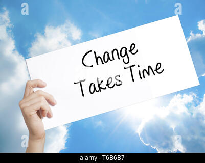 Change Takes Time Sign on white paper. Man Hand Holding Paper with text. Isolated on sky background. Stock Photo