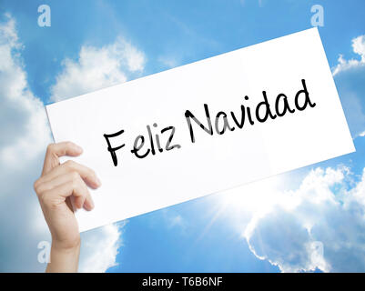 Feliz Navidad  (Merry Christmas In Spanish) Sign on white paper. Man Hand Holding Paper with text. Isolated on sky background Stock Photo