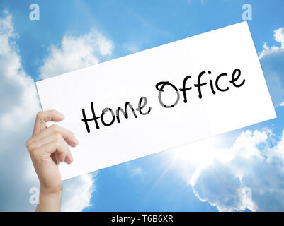 Home Office Sign on white paper. Man Hand Holding Paper with text. Isolated on sky background Stock Photo