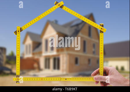 shell of house under construction with folding ruler in hand of real estate agent Stock Photo