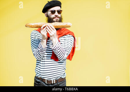Portrait of a stylish man dressed in french style with striped shirt, hat and red scarf on the yellow background Stock Photo