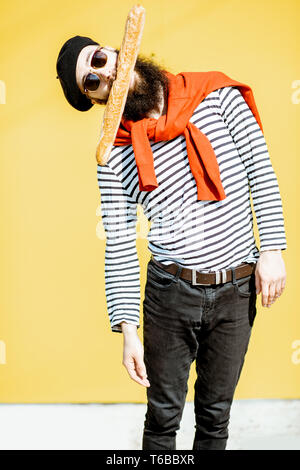 Portrait of a stylish man dressed in french style with striped shirt, hat and red scarf on the yellow background Stock Photo