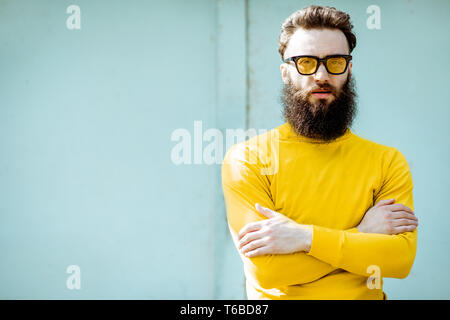 Portrait of a confident stylish bearded man in yellow sweater on the turquoise background outdoors Stock Photo