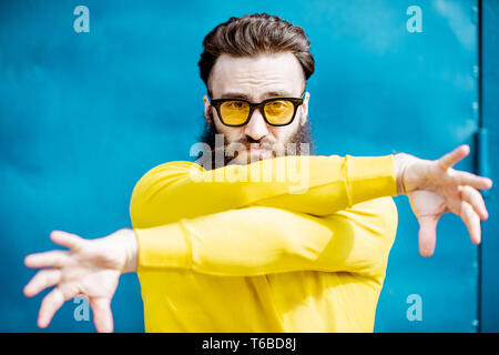 Portrait of a stylish bearded man in yellow sweater and sunglasses on the blue background Stock Photo