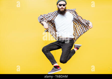 Portrait of a cool stylish man in checkered shirt jumping on the bright yellow background Stock Photo