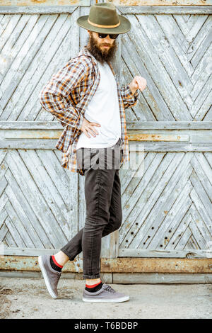 Portrait of a stylish man in checkered shirt and hat on the wooden gate background outdoors Stock Photo