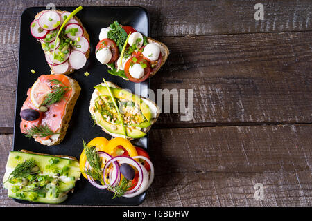Sandwiches or tapas prepared with cream cheese , vegetables and salmon, over old wooden background. Healthy food for lunch or breakfast. Horizontal im Stock Photo