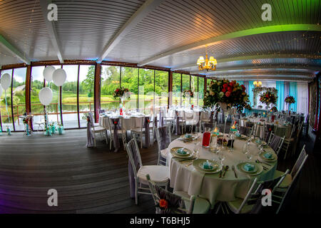 Luxury decorated place for wedding reception catering in restaurant next to the pond. Guest tables in luxury decorated wedding banquet room. Festive d Stock Photo