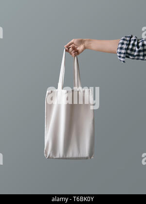 Eco-friendly product Zero waste concept A girl is holding a white blank canvas tote bag against a gray wall background Stock Photo