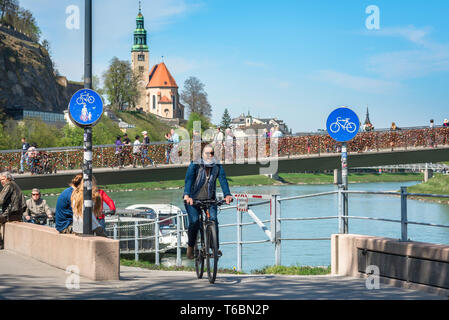 Woman cycling, view of a young woman cycling along a cycle path in the city of Salzburg with the Makartsteg bridge in the background, Austria.