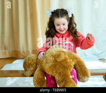 Angry little girl beating her teddy bear - domestic abuse concept. Girl 4-5 year old punishes toy bear. Stock Photo