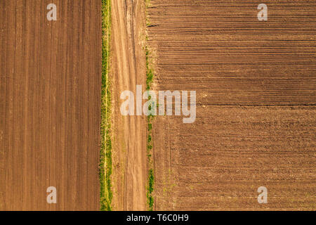 Aerial view of dirt road through countryside and agricultural field from drone pov, top down perspective Stock Photo