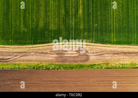 Aerial view of dirt road through countryside and agricultural field from drone pov, top down perspective Stock Photo