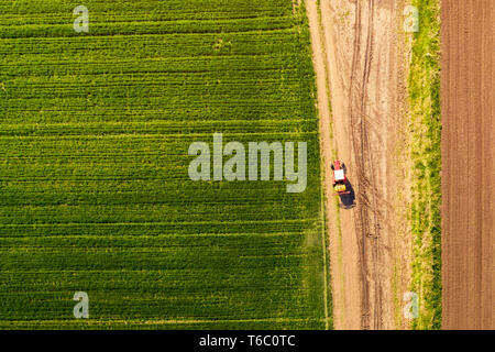 Aerial view of tractor with attached crop sprayer on countryside dirt road heading toward the field, top down view from drone pov Stock Photo