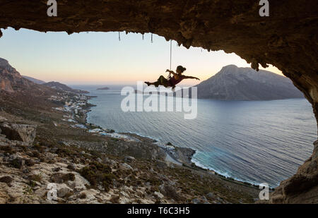 Young female rock climber hanging on rope and stretching out arms. Rock climber relaxing or fooling around while being lowered down against picturesqu Stock Photo