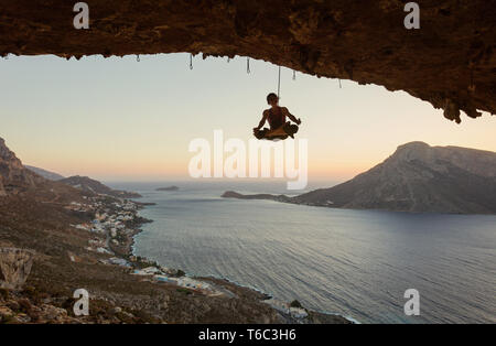 Young female rock climber hanging on rope in asana position. Rock climber having fun and fooling around while being lowered down. Stock Photo