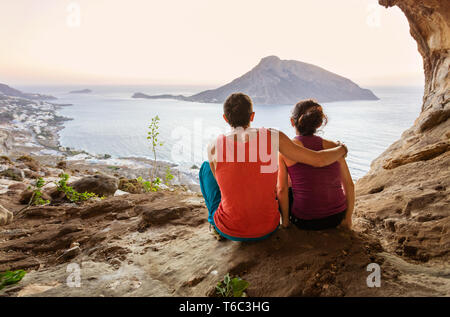 Couple of rock climbers having rest while sitting at bottom of cliff and enjoying picturesque view of Telendos Island in front. Kalymnos Island, Greec Stock Photo