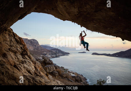 Rock climber hanging on rope after falling of cliff, climbing in cave at sunset Stock Photo