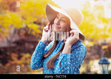 Beautiful young woman walking in autumn park. Gorgeous young woman in fall with big hat, smiling and enjoying nature Stock Photo