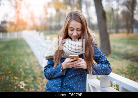 Happy young woman using a smart phone during the walk in autumn city park. Stock Photo