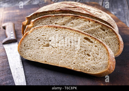 Freshly backed Farmhouse Bread sliced as close-up on an old burnt cutting board Stock Photo