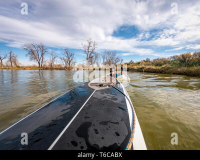 male paddler swimming behind a stand up paddleboard a lake in Colorado, bow view Stock Photo