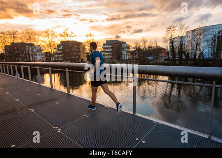 Young athletic man practicing sport outdoors, running fast along bridge over the sunset sky background. Self overcome conquering obstacles and win. He Stock Photo