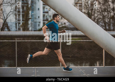 Young athletic man practicing sport outdoors, running fast along bridge. Self overcome conquering obstacles and win. Healthy lifestyle concept. Workou Stock Photo