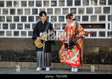 KURASHIKI, JAPAN - MARCH 31, 2019: Young man and a girl in kimono dress imitate playing on electric guitars against the background of a traditional wa Stock Photo