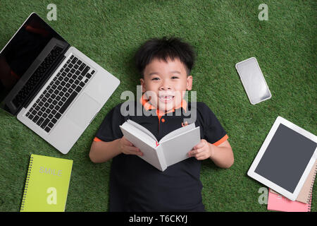 seven years old child reading a book lying on the grass Stock Photo