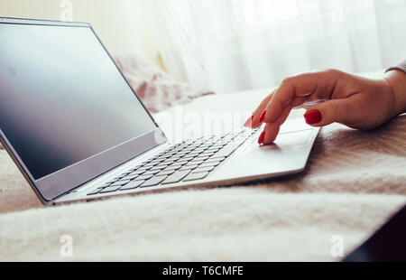 Womans hand with red nails on laptop keyboard, lady using laptop on bed blanket, close-up Stock Photo