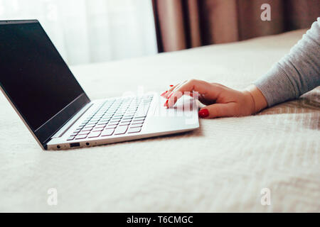 Womans hand with red nails on laptop keyboard, lady using laptop on bed blanket, close-up Stock Photo