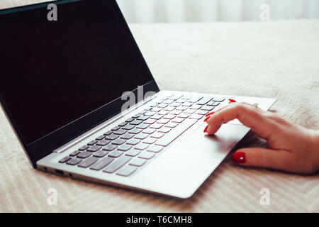 Womans hand with red nails on laptop keyboard, lady using laptop on bed blanket, close-up Stock Photo