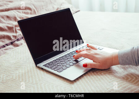 Womans hand with red nails on laptop keyboard, lady using laptop on bed blanket, close-up Stock Photo