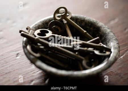 A small enamel bowl filled with antique keys sitting on a cherry wood table. Stock Photo