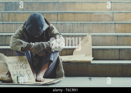 Homeless. Unhappy homeless man with black gloves is holding hand to get bit coins or help food donation from the people. Stock Photo