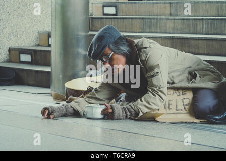 Homeless. Unhappy homeless man with black gloves is holding hand to get bit coins or help food donation from the people. Stock Photo