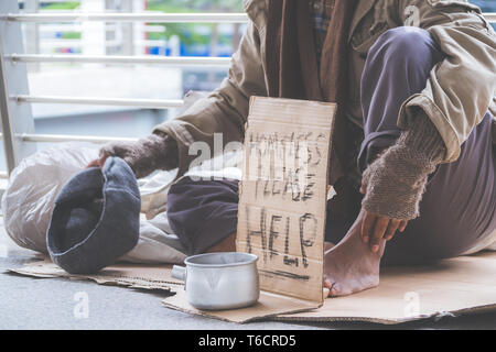 Homeless. Unhappy homeless man with black gloves is holding hand to get bit coins or help food donation from the people. Stock Photo