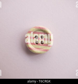 Isolated wooden button with colored colorful stripes on a light pink background, sewing Stock Photo