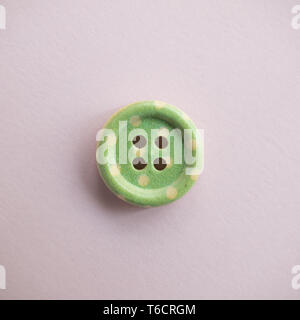 Isolated wooden button with colored colorful dots on a light pink background, sewing Stock Photo