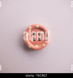 Isolated wooden button with colored colorful dots on a light pink background, sewing Stock Photo