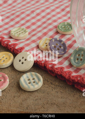 Wooden buttons with colored stripes of colors on a red and white checkered tablecloth, sewing Stock Photo