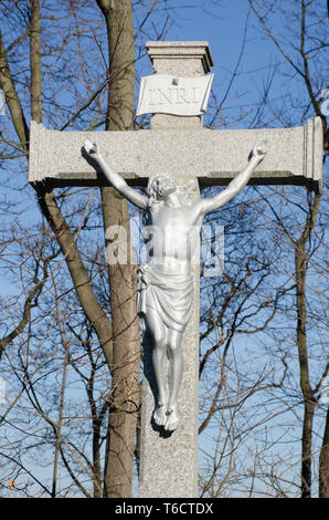 Stone statue of Christ on the cross against a blue sky at a cemetery in ...